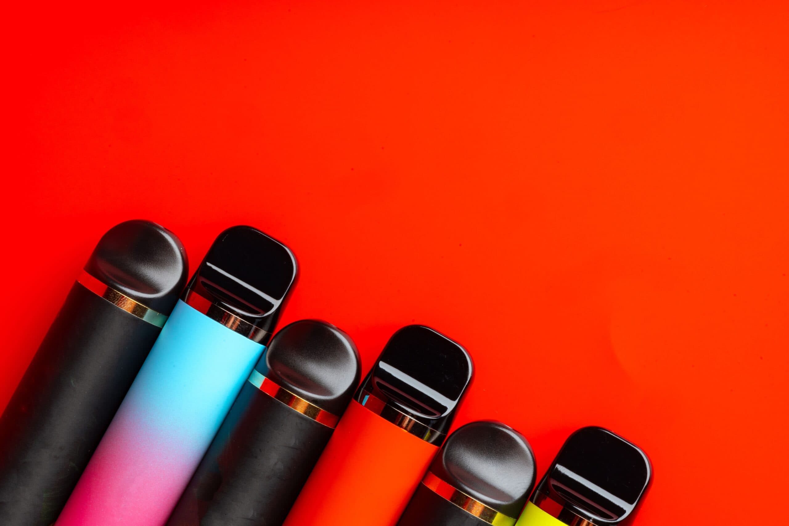 Colorful disposable vapes lined up on a bold red background, representing popular flavour options.