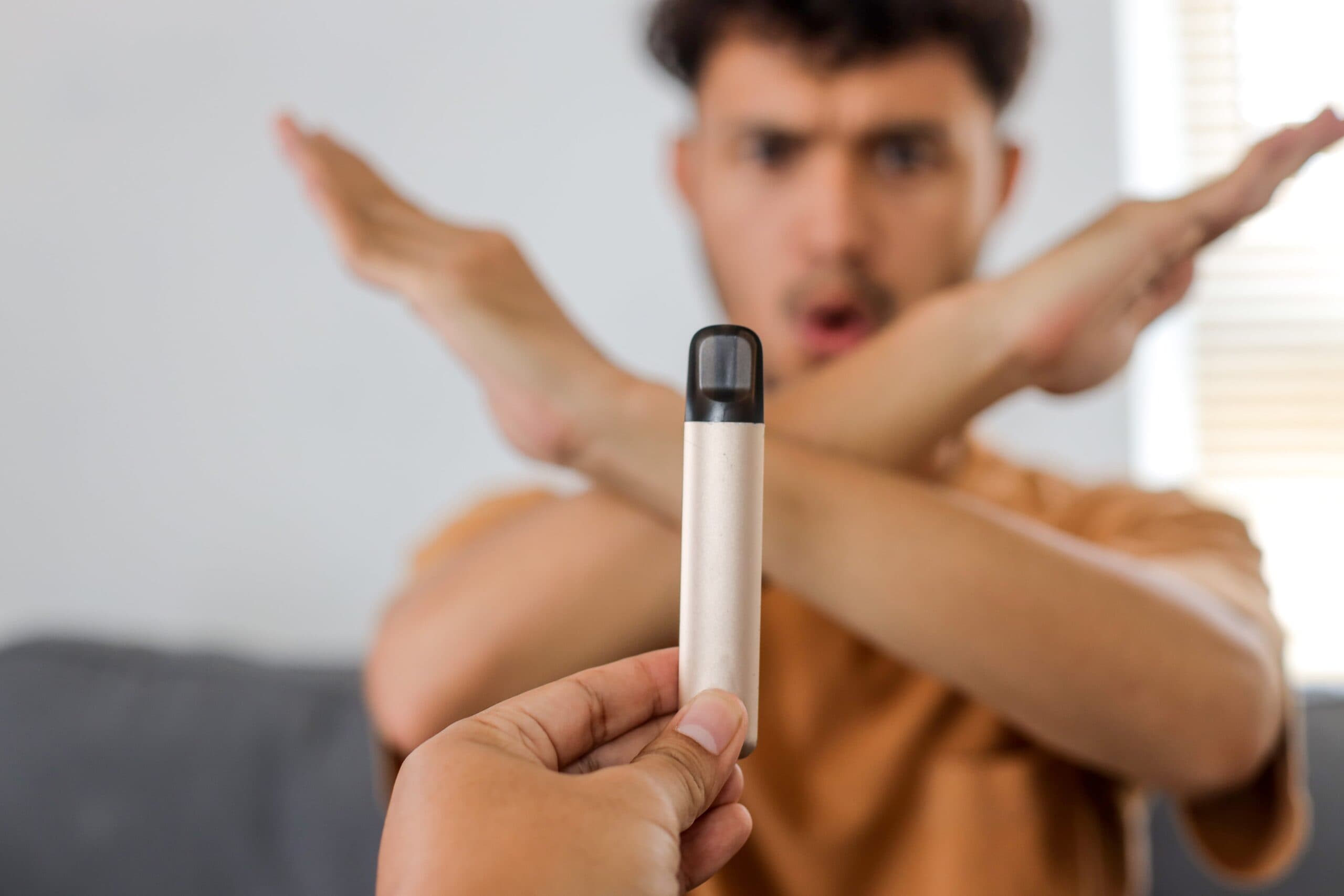 A person rejects a disposable vape by crossing their arms in an "X" gesture, refusing the device being offered.
