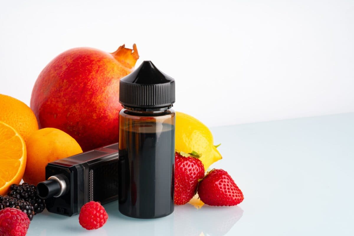 Nicotine salt e-liquid bottle surrounded by fresh fruits including pomegranate, orange, lemon, strawberries, and raspberries, with a vape device in the background.