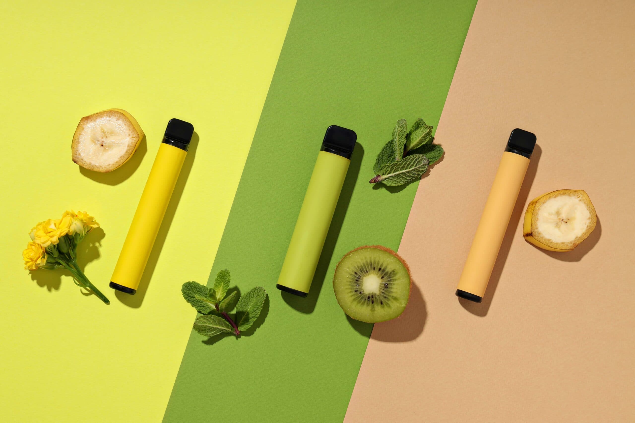 Colourful disposable vapes with fruit slices representing vibrant vape flavours, including banana, kiwi, and mint.