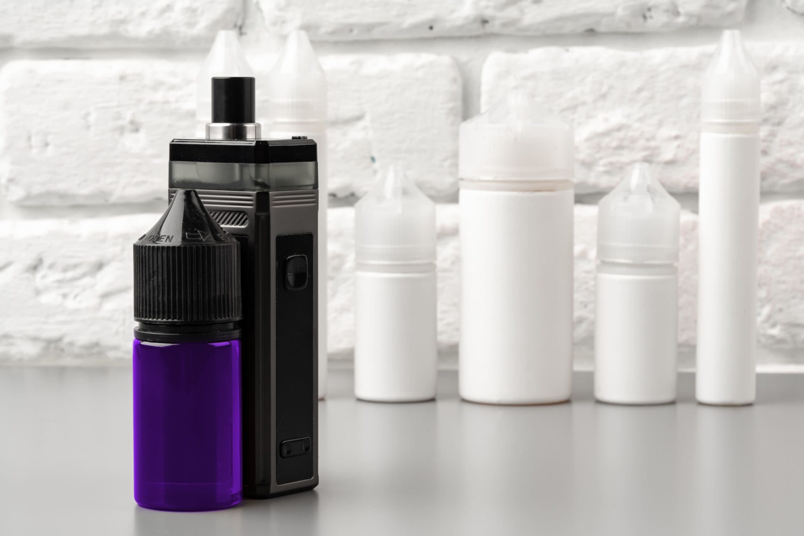 Vape juice bottle next to vaping device, showcasing e-liquid bottle types used for vaping.