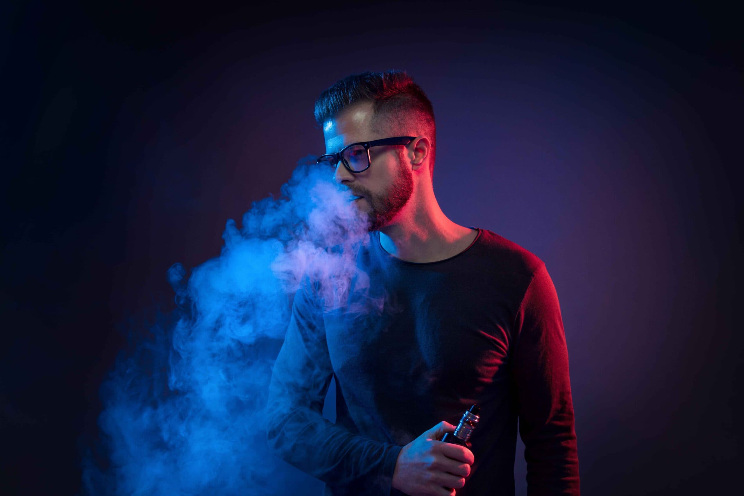 Man vaping e-cigarette with blue smoke in a dark setting.