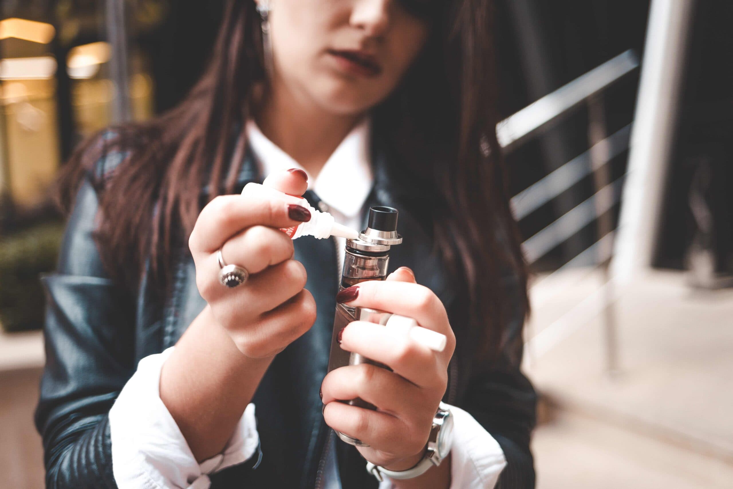Woman holding vape device with vape juice outdoors, showcasing vaping lifestyle.